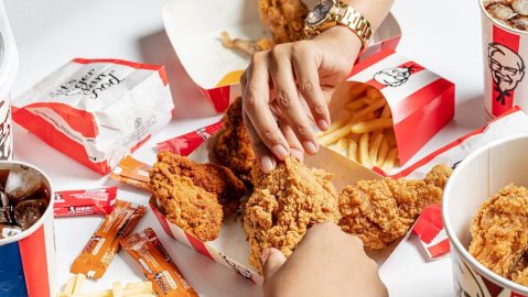 Manos se acercan para tomar una pieza de pollo de KFC.