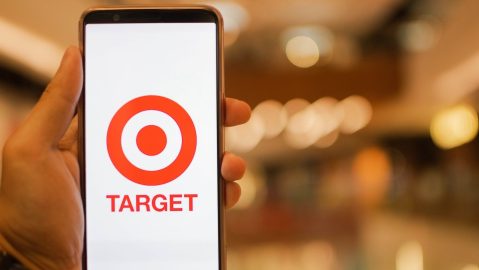 Mano sosteniendo un teléfono inteligente que muestra la aplicación Target con un centro comercial de fondo.