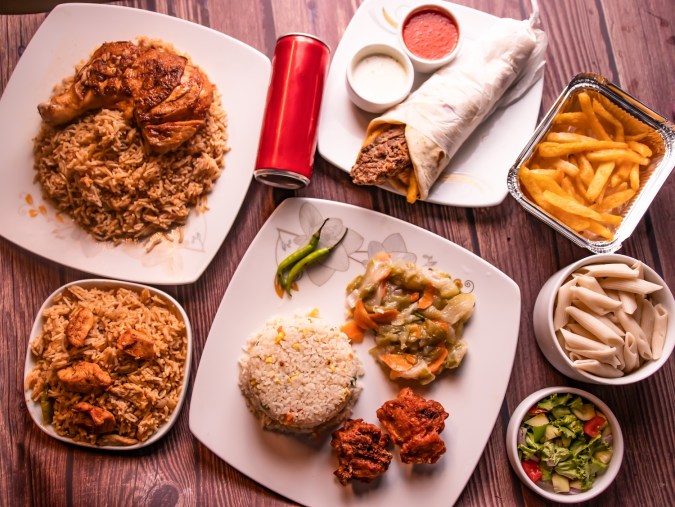 Mesa de comida rápida variada: seekh kabab y tikka biryani, arroz frito, pollo frito, shawarma seekh kabab, bebida, papas fritas, raita y ensalada, vista superior de la mesa de madera.
