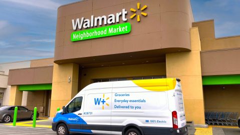 Vista exterior de la tienda Walmart Neighborhood Market con camioneta de reparto eléctrica Walmart+ estacionada en la entrada.