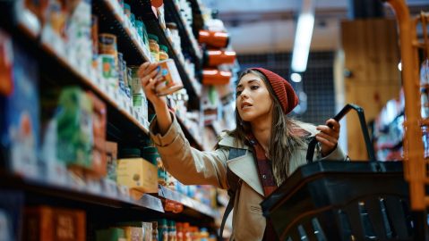 Mujer joven comprando comida enlatada en una tienda de comestibles.