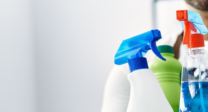 Joven hispano sosteniendo productos de limpieza en casa.