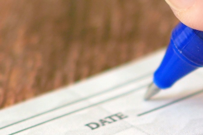 Firma a mano de un cheque bancario sobre fondo de mesa de madera.