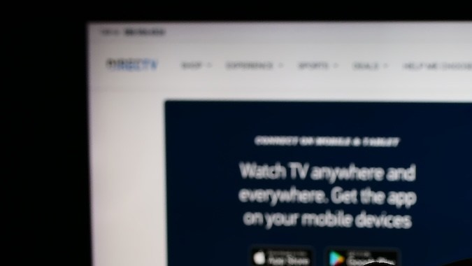 Persona que sostiene un teléfono móvil con el logotipo de la distribuidora de televisión estadounidense DirecTV LLC frente a la página web de la empresa.