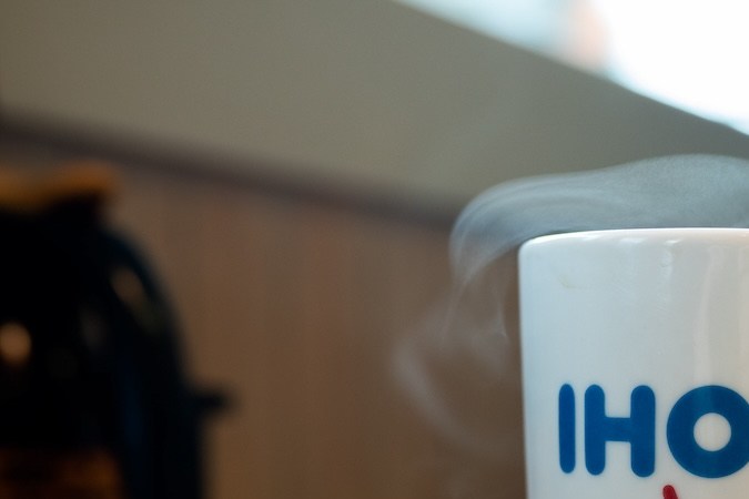 Taza Ihop con café caliente sobre una mesa con vapor saliendo de ella.