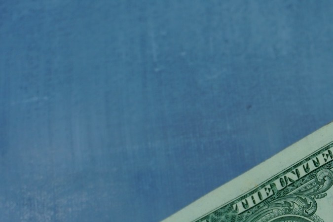 Una mano sosteniendo dos billetes de un dólar.