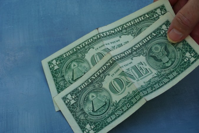 Una mano sosteniendo dos billetes de un dólar.