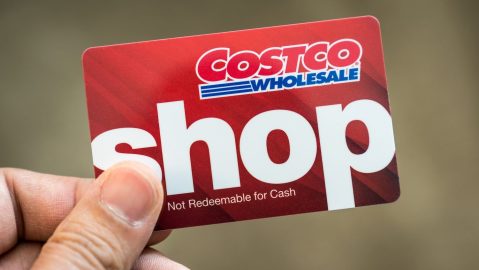 Mano sosteniendo una tarjeta de regalo de color rojo de Costco Wholesale aislada.