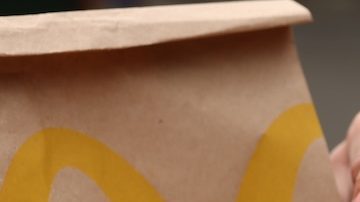 Mujer con menú de McDonald's en una mesa de madera al aire libre, primer plano.