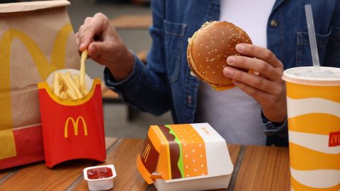 Mujer con menú de McDonald's en una mesa de madera al aire libre, primer plano.