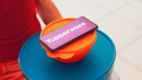 En esta ilustración fotográfica, una persona lleva varios productos de plástico (envases) y un teléfono inteligente muestra el logotipo de Tupperware.