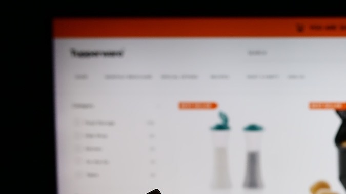 Persona que sostiene un teléfono inteligente con el logotipo de la empresa estadounidense de productos para el hogar Tupperware Brands Corporation frente a un sitio web.