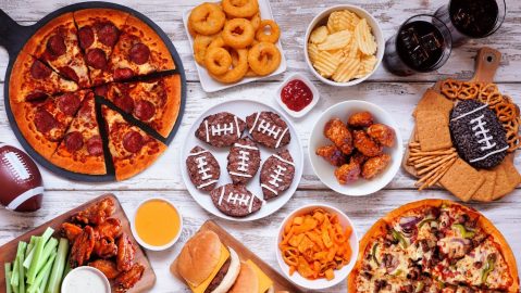 Mesa de comida con temática de fútbol o Super Bowl. Pizza, hamburguesas, alitas, bocadillos y guarniciones.
