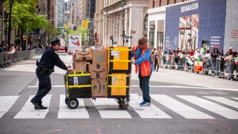 Un oficial de policía de Nueva York ayuda a un trabajador de Amazon a cruzar Madison Avenue en Nueva York durante un desfile.