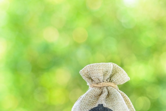 Una pareja de ancianos en miniatura de pie sobre una balanza básica con una bolsa de dinero en dólares estadounidenses.