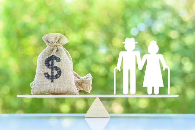 Una pareja de ancianos en miniatura de pie sobre una balanza básica con una bolsa de dinero en dólares estadounidenses.