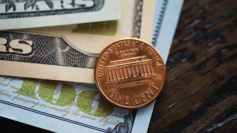 Primer plano de moneda estadounidense: moneda de un centavo y billetes de dólar sobre superficie de madera.