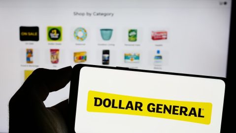 Persona que sostiene un teléfono móvil con el logotipo de la empresa minorista estadounidense Dollar General Corporation en la pantalla frente a una página web.