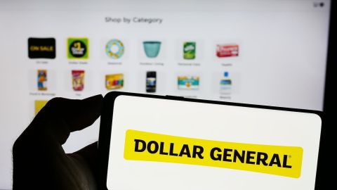 Persona que sostiene un teléfono móvil con el logotipo de la empresa minorista estadounidense Dollar General Corporation en la pantalla frente a una página web.