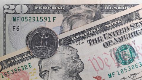 Primer plano de una moneda de cuarto de dólar encima de un billete de 10 y 20.