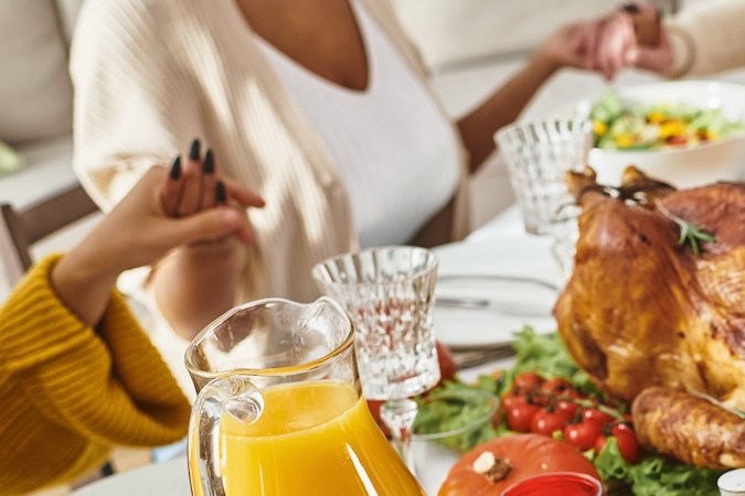 Vista recortada de una familia multiétnica rezando junta en una mesa festiva con pavo y vino, Acción de Gracias.