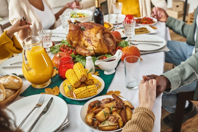 Vista recortada de una familia multiétnica rezando junta en una mesa festiva con pavo y vino, Acción de Gracias.