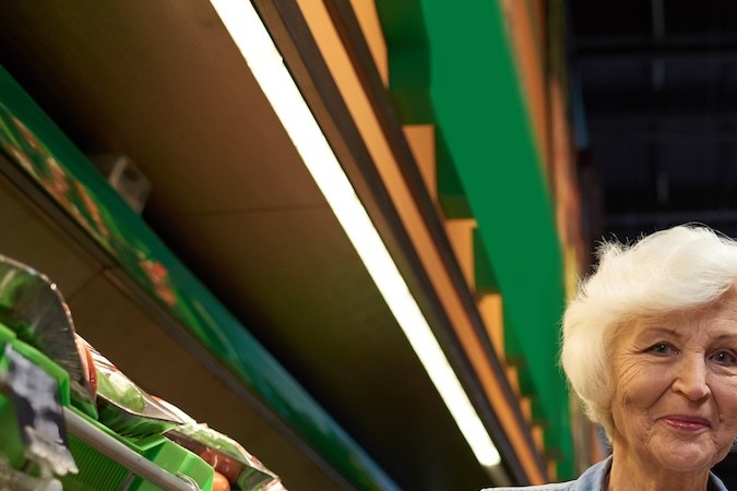 Retrato de una pareja mayor moderna con carrito de compras posando y mirando a la cámara en el supermercado mientras disfruta de las compras.