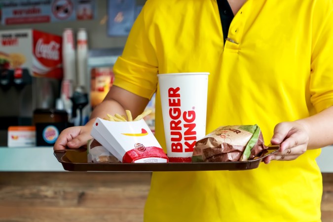 Un hombre que sostiene una bandeja con un juego de Burger King tiene papas fritas tipo hamburguesa Whopper y un vaso de papel con bebida de cola en el autoservicio del restaurante Burger King.