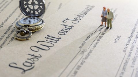 Concepto de legado, herencia o impuesto sobre la muerte como testamento o última voluntad: una pareja de ancianos en miniatura se encuentra de pie sobre un formulario de documento legal y se prepara para transferir propiedades a sus herederos después de la muerte.
