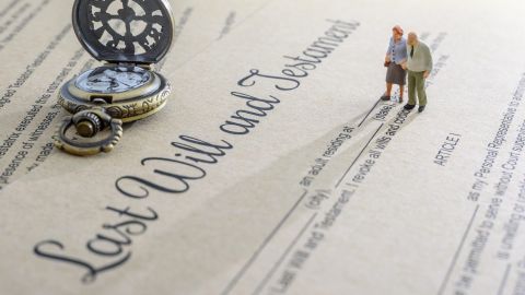 Concepto de legado, herencia o impuesto sobre la muerte como testamento o última voluntad: una pareja de ancianos en miniatura se encuentra de pie sobre un formulario de documento legal y se prepara para transferir propiedades a sus herederos después de la muerte.
