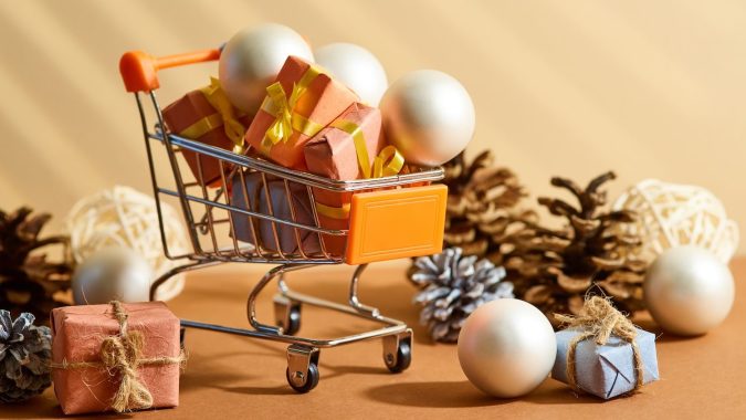 Composición a partir de un carrito con regalos, piñas y adornos navideños. Descuentos de Navidad y Año Nuevo, compras, promociones, rebajas, compras online, publicidad empresarial.