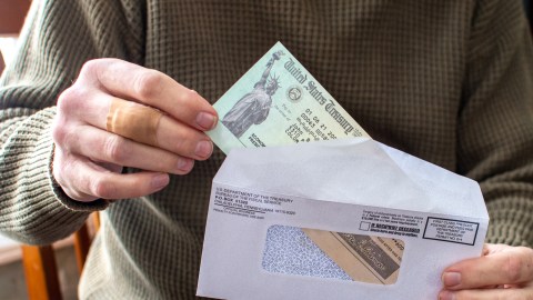 Sobre muestra a una persona sacando un cheque de estímulo, que es un alivio económico